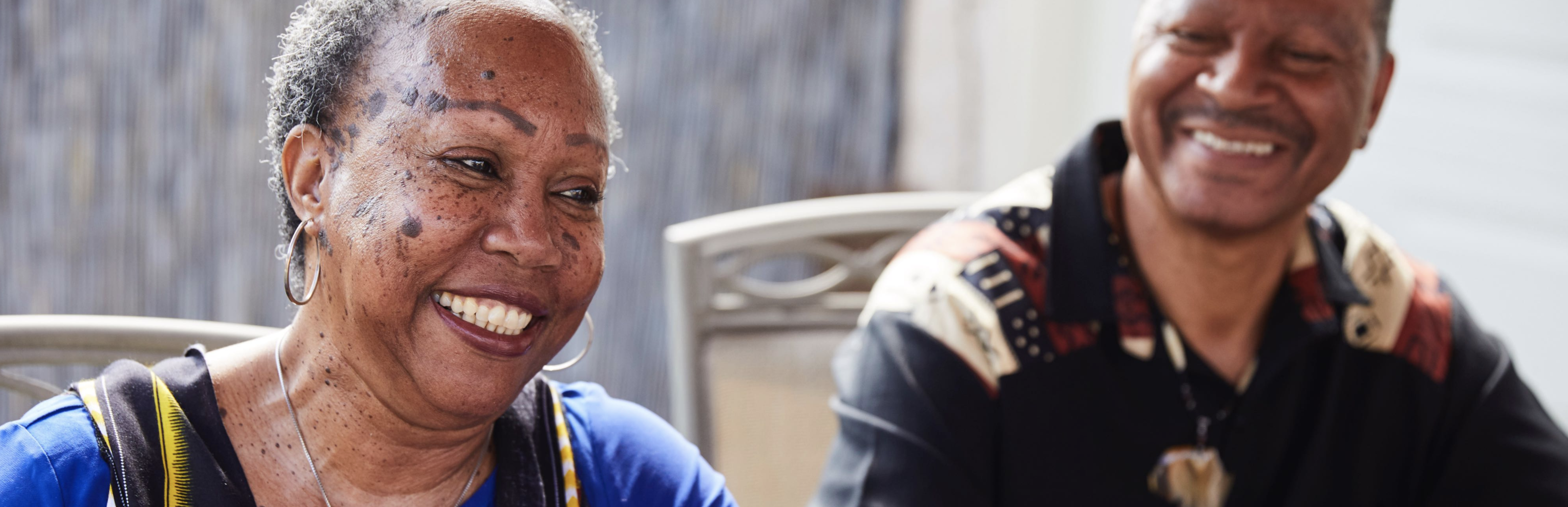 Older Black woman smiling on left, out of focus smiling Black man on right