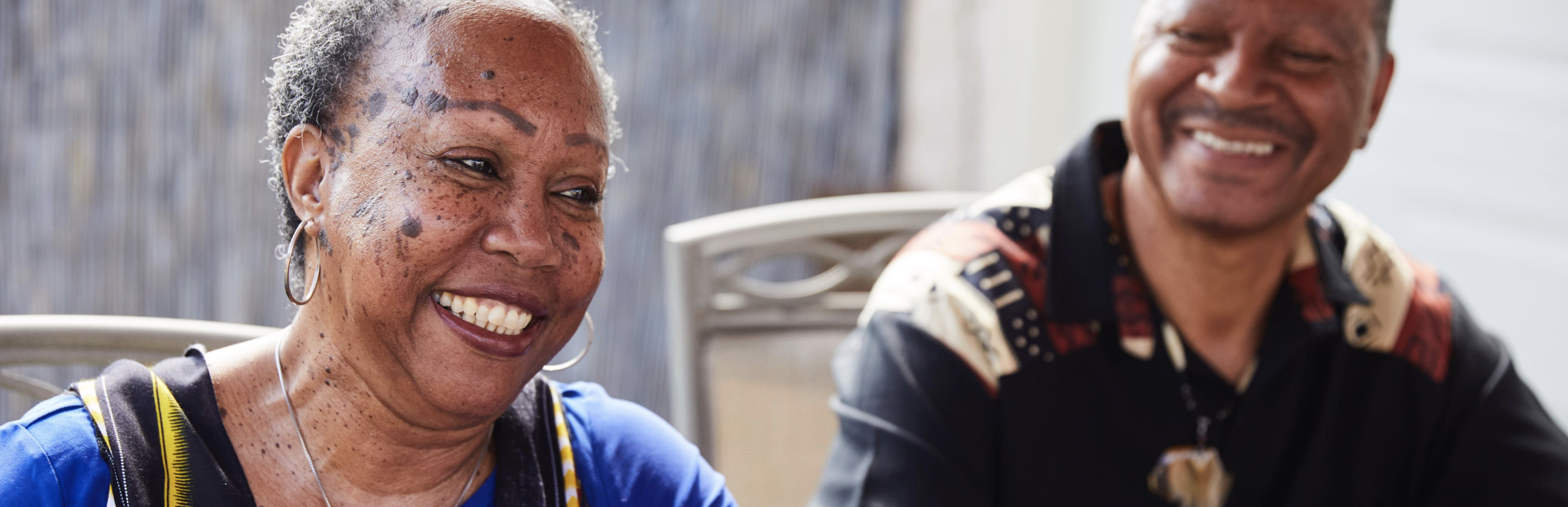 Mujer mayor de color sonriendo a la izquierda, hombre de color fuera de foco sonriendo a la derecha