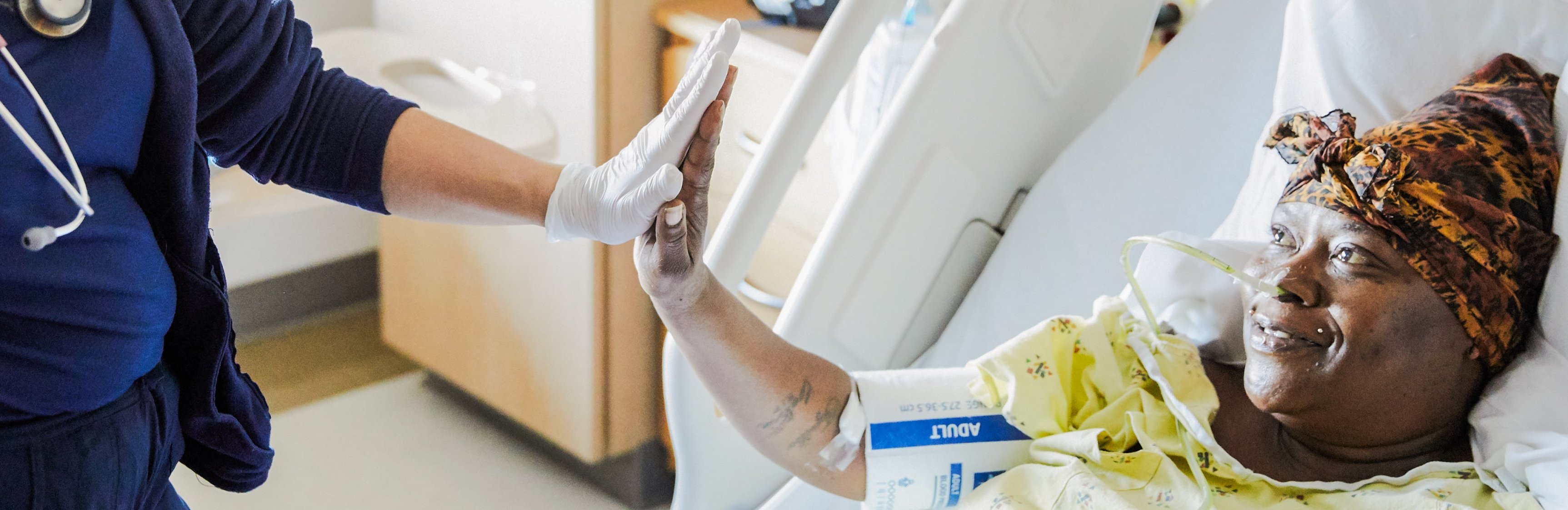 Black female patient in hospital bed high-fiving a nurse's gloved hand