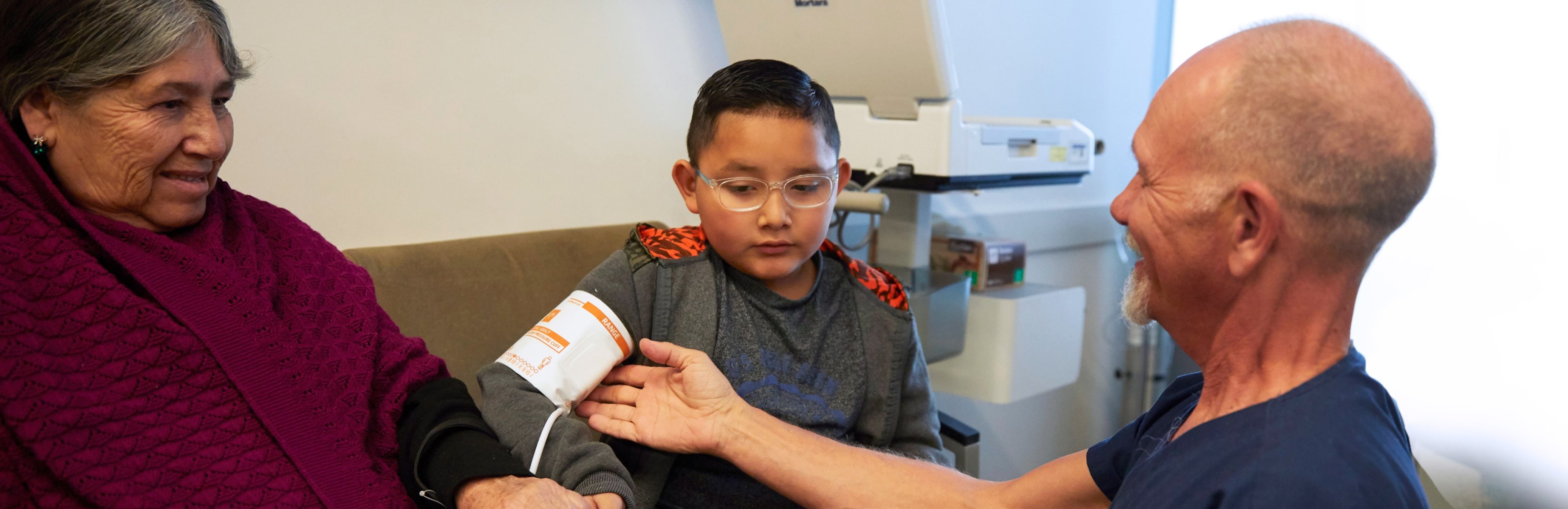 White male nurse taking blood pressure cuff off young Latino boy as his family member looks on