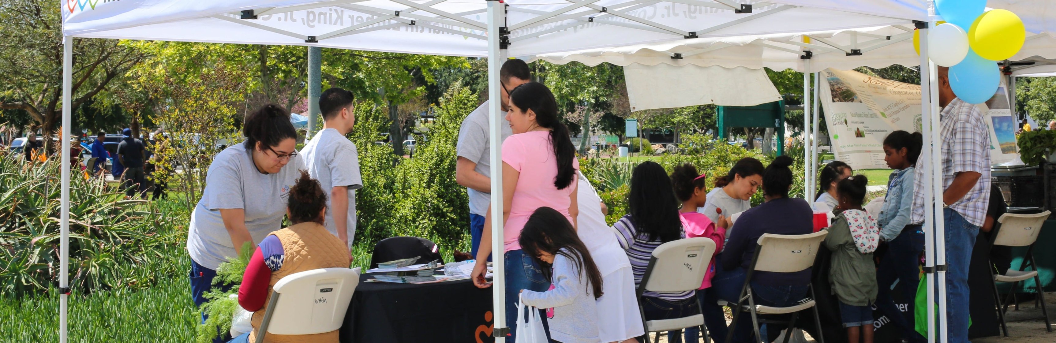 Miembros de la comunidad del sur de LA sentados bajo un gazebo y hablando con los trabajadores de la salud de la comunidad