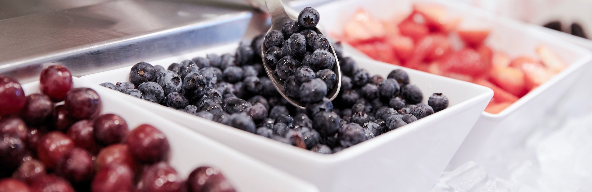 Close up of hand scooping blueberries at a salad bar