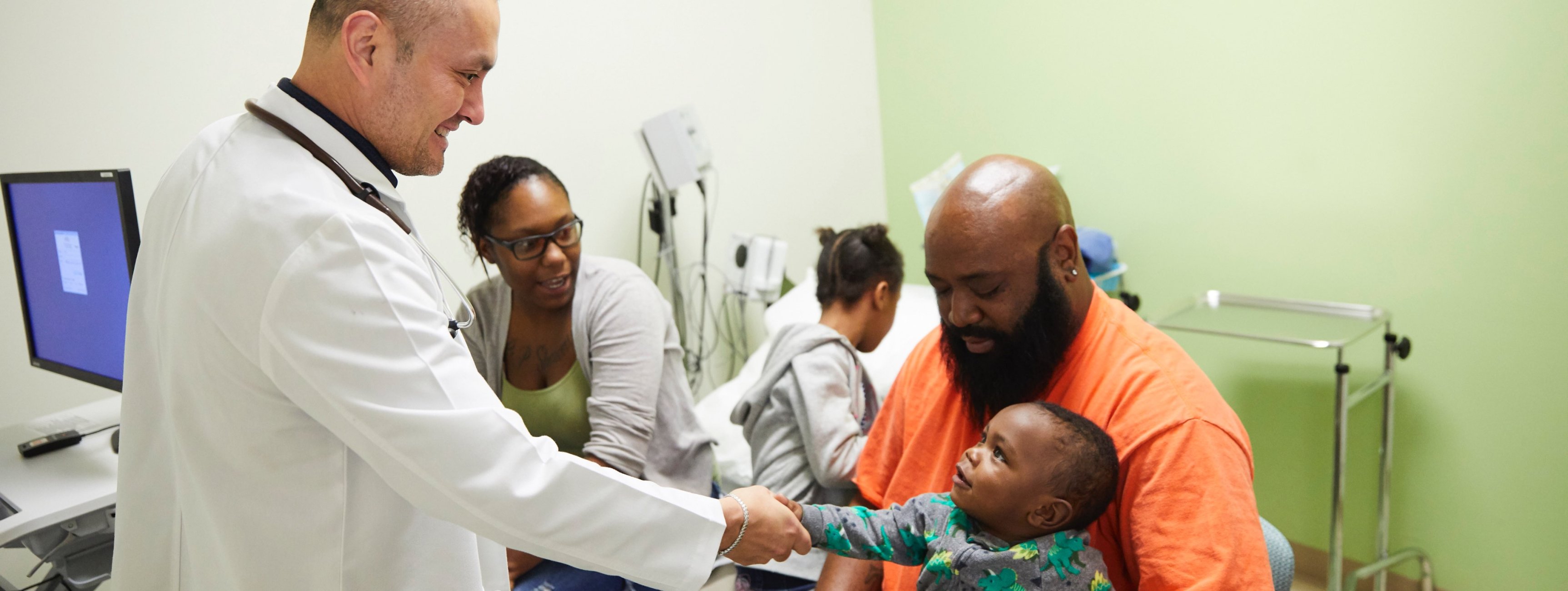 Latino doctor holding hand of Black baby sitting in father's lap as mother looks on 