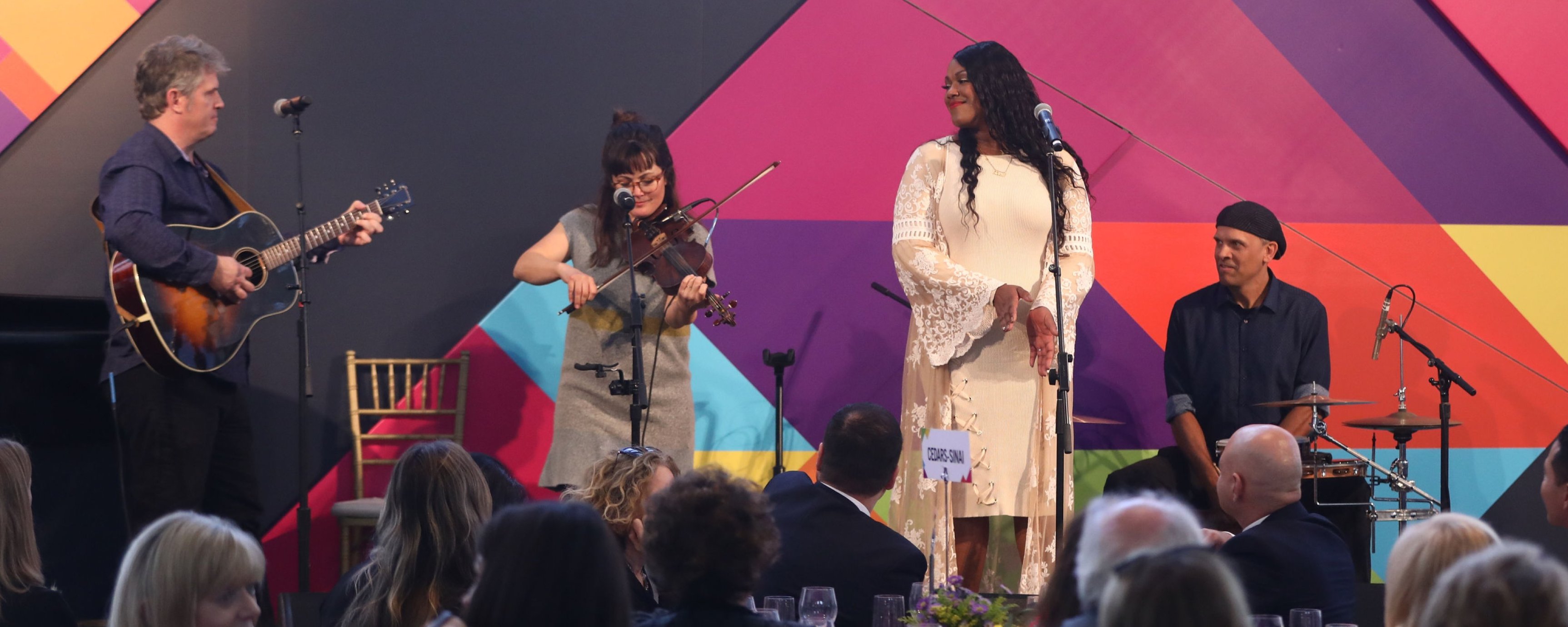 Group shot of four musicians standing in front of colorful backdrop on stage