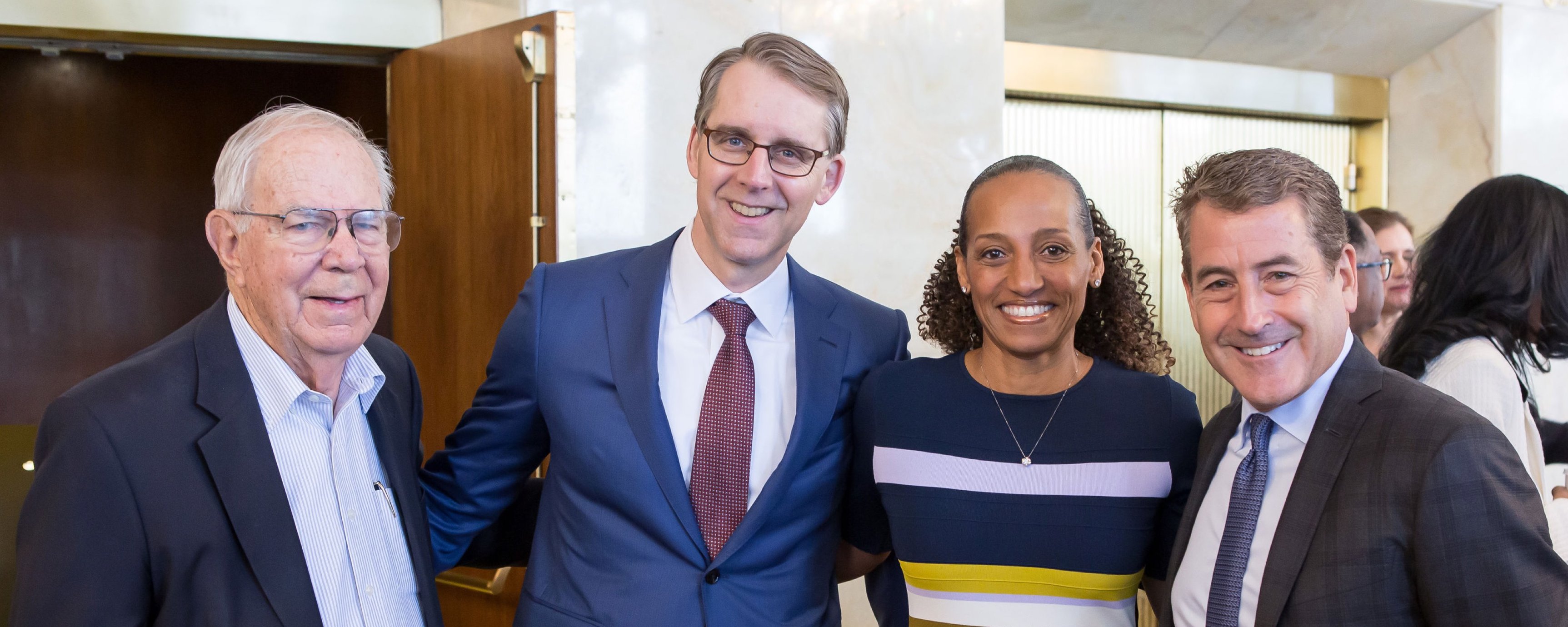 Group shot of three white men and one Black woman standing together at the event