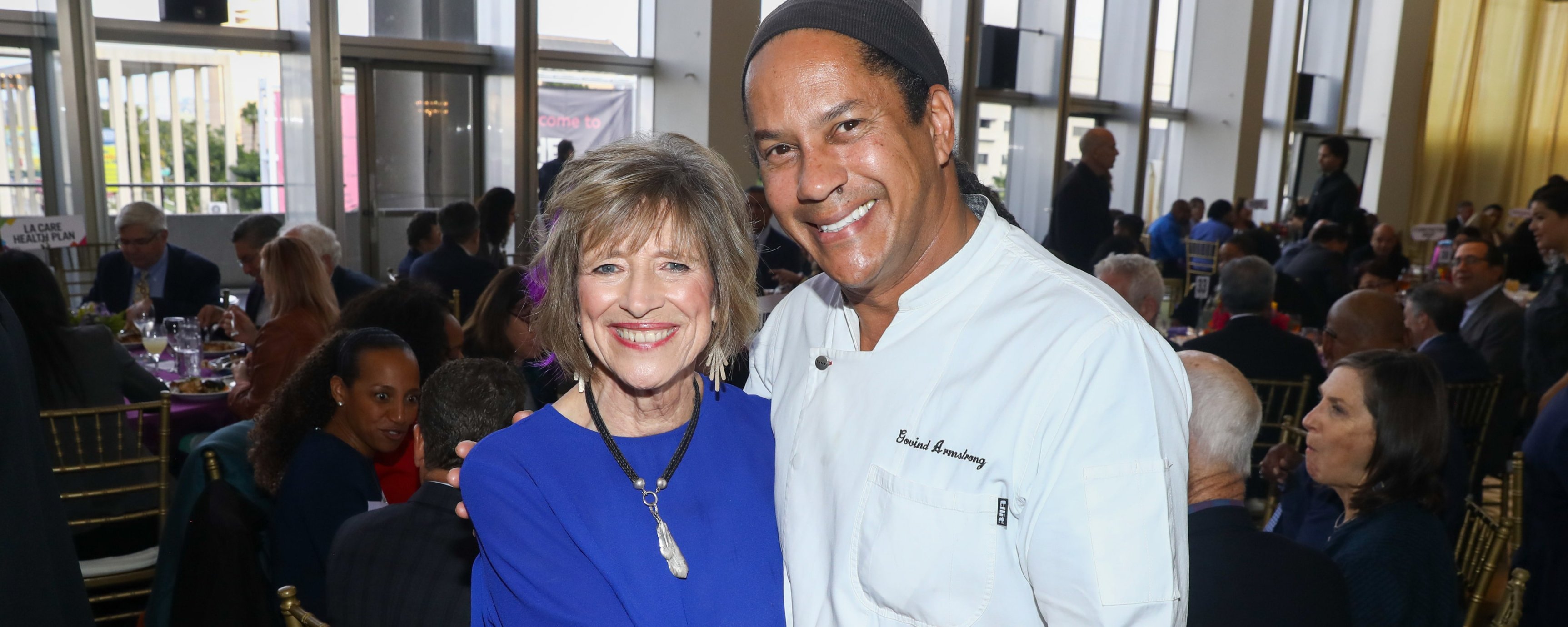 Dyan Sublett, an older white woman, standing with Chef Govind Armstrong, a middle-aged Afro-Caribbean man at the event