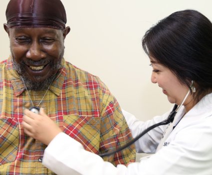 Asian female doctor using stethoscope on Black male patient's chest