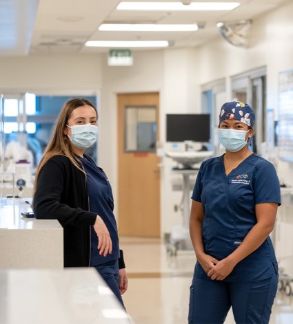 Latina and Filipina nurse stand across from each other in the ICU
