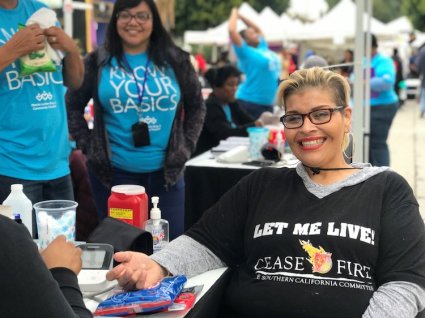 Mujer latina sonriente con cabello corto recibiendo un examen médico en el evento Conozca lo Básico