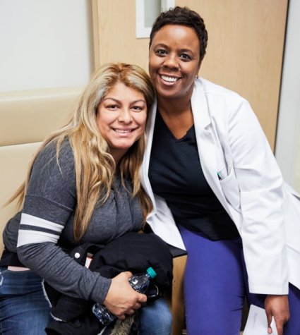 Black female nurse sitting side by side with female patient smiling