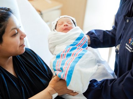 Nurse handing newborn baby to Latina mother