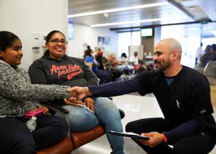 Latino doctor reaching out to hold hands with young Latina patient in Emergency Room waiting room