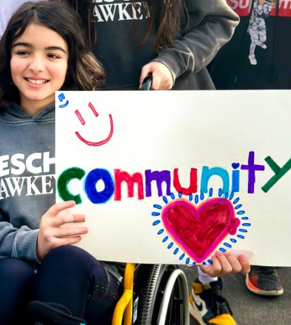 Little girl sitting in in a wheelchair holding a sign that says "community"