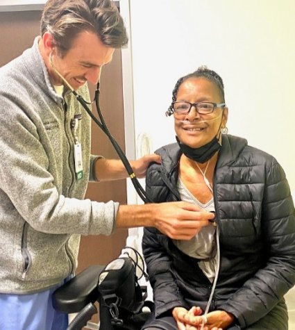 Older African American woman sitting with a white male doctor holding a stethiscope up to her chest