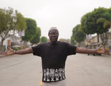 Photo of Aziz standing in the street with his arms outstretched to his sides