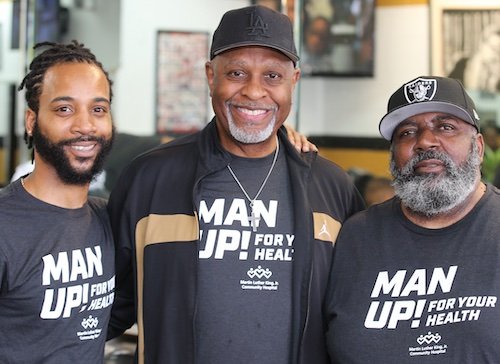 Tres hombres de color de diferentes edades sonriendo usando camisetas negras que dicen ¡Man Up!
