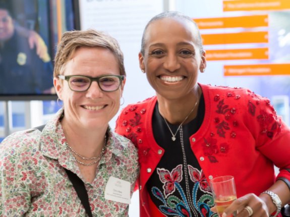 Mujer blanca de mediana edad sonriendo al lado de una mujer afroamericana de mediana edad en un evento