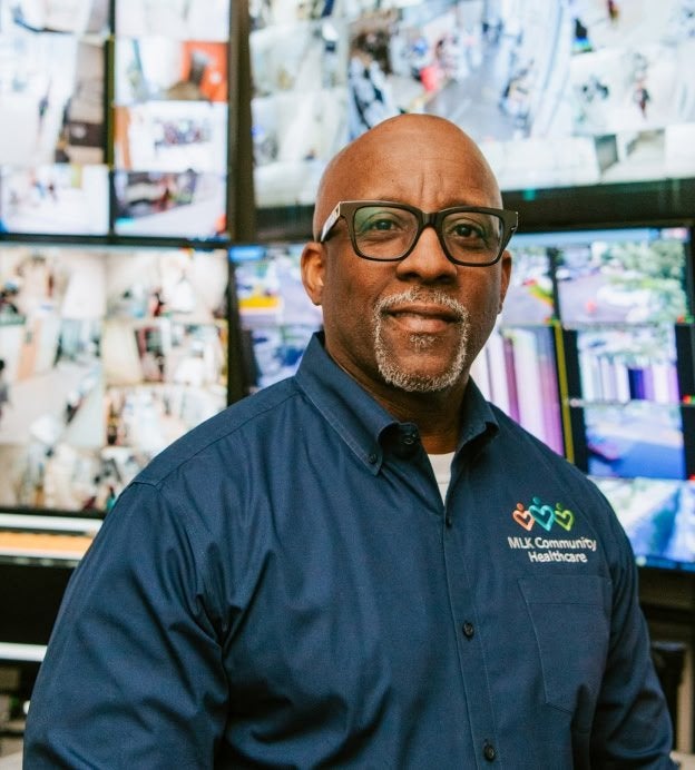 Black man smiling in front of computer monitors