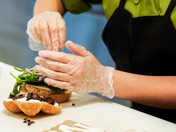 Close up of gloved hands preparing a sandwich