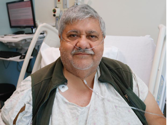 Older Latino man with oxygen tubes smiling while sitting on hospital bed