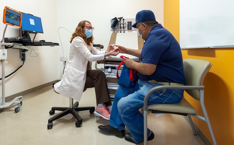 Female doctor hands prescription bottle to male patient