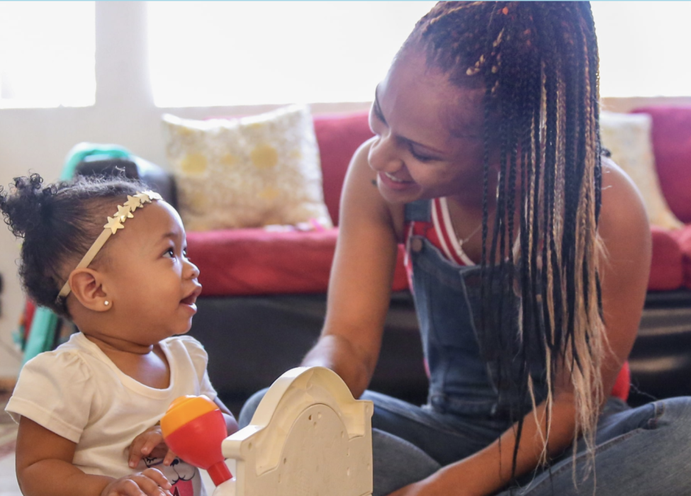 Black mother smiling and playing with young daughter on a rug