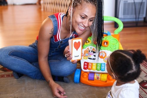 Young Black mother showing her infant daughter a card that says heart