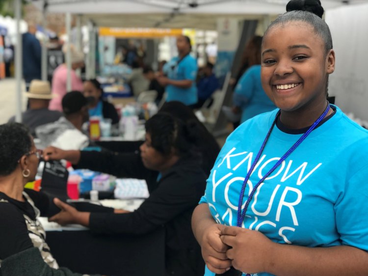 Mujer de color sonriendo y usando una camiseta azul de Conozca lo Básico