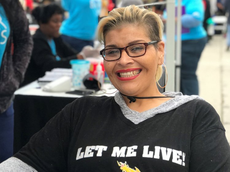 Smiling Latina patient in a black shirt reading let me live!