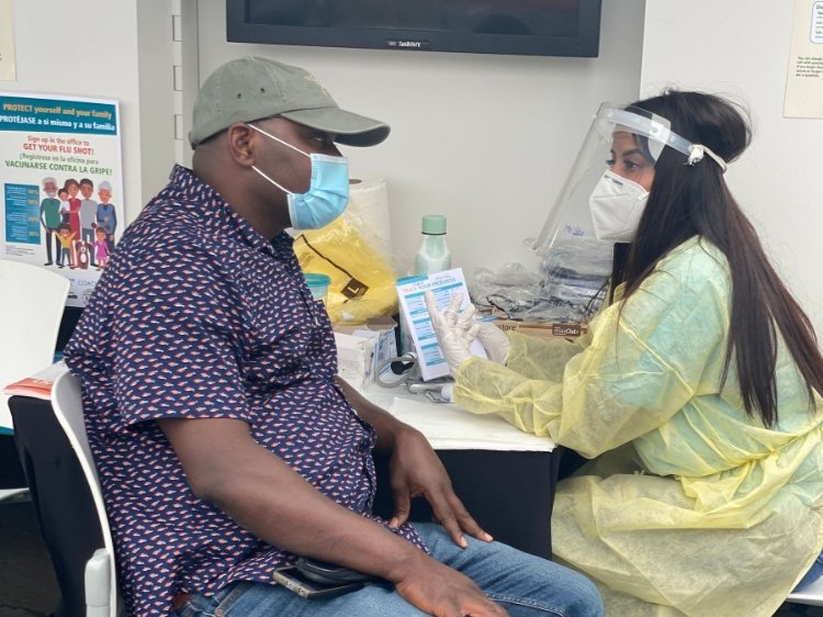 Latina nurse in full PPE speaking to Black male patient at an outdoor health event