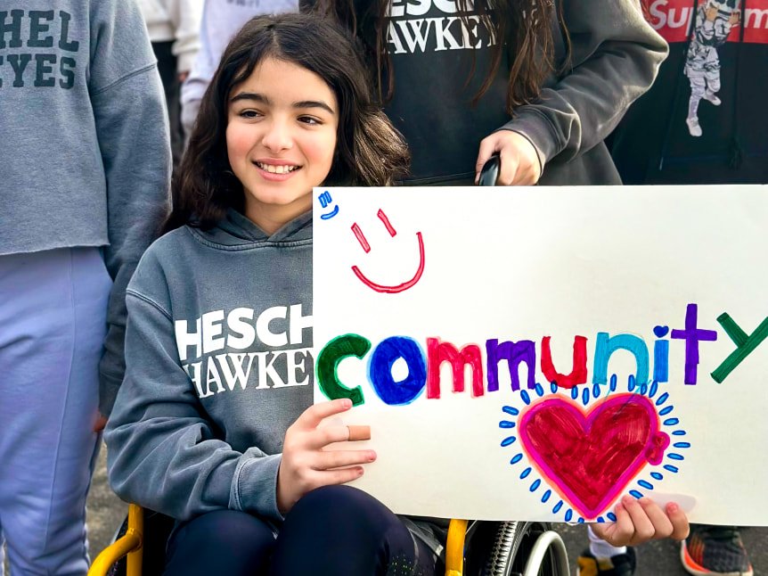 Little girl sitting in a wheelchair holding a sign that says "community"