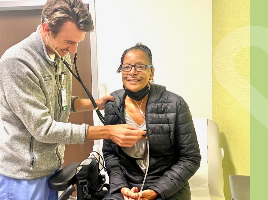 Older African American woman sitting with a white male doctor holding a stethiscope up to her chest